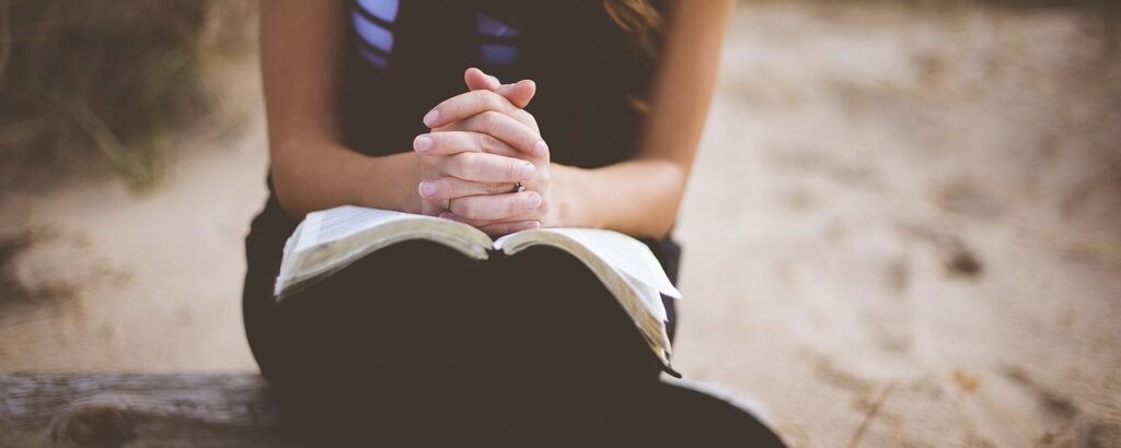 Eine Frau, die Hände zum Gebet über der Bibel gefaltet.